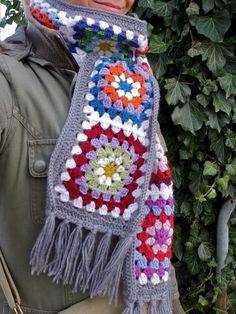 a woman is wearing a crocheted scarf with fringes and flowers on it