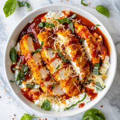 a white bowl filled with pasta and sauce on top of a marble counter next to basil leaves