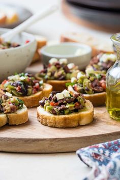 several pieces of bread with olives and other toppings on a wooden cutting board