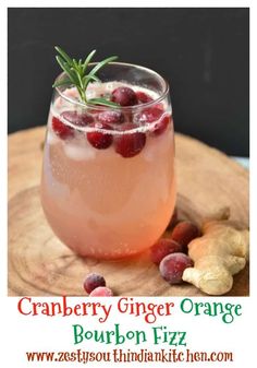 a drink with cranberries and rosemary garnish sits on a wooden cutting board