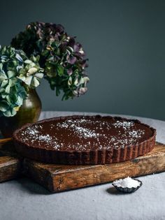 a chocolate tart sitting on top of a wooden cutting board next to a vase with flowers