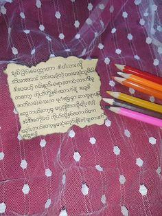 several pencils are sitting next to a piece of paper on a lace covered tablecloth