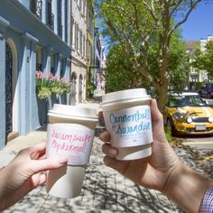 two people holding up coffee cups on the street