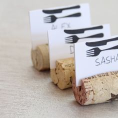 three wine cork place cards with forks and spoons on them sitting next to each other