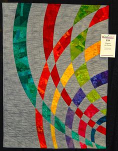 a colorful quilt is hanging on the wall in front of a white tablecloth with multicolored circles