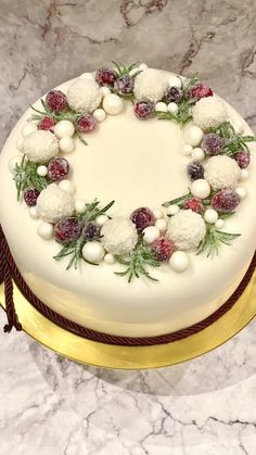 a white cake decorated with berries and greenery on a gold plated platter