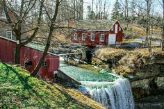 a red house with a waterfall in the foreground and a bridge over water below it