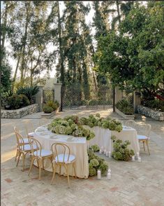 an outdoor dining area with tables and chairs covered in white tablecloths, surrounded by trees