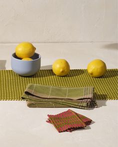 three lemons in a blue bowl and two napkins on a mat next to each other