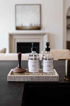 two bottles of hand soap and a brush on a tray in front of a fireplace