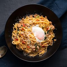 a black plate topped with pasta and an egg on top of it next to a spoon