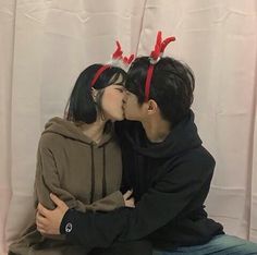 a man and woman kissing each other while wearing reindeer antlers on their heads in front of a white backdrop