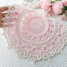 pink doily with white crochet lace on top and flowers in the background