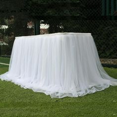 the table is covered with white cloths and sits on green grass in front of a tennis court