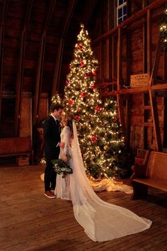 a bride and groom standing in front of a christmas tree at their barn wedding venue