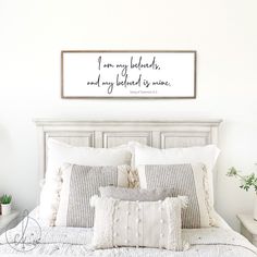 a bed with white sheets and pillows in a bedroom next to a wall mounted quote