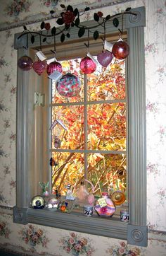 a window with ornaments hanging from it's side and an autumn scene in the background