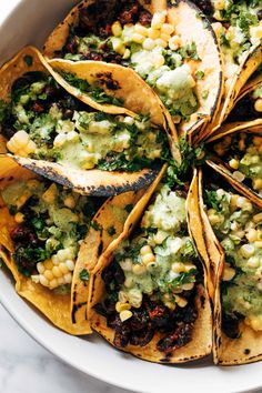 a white bowl filled with tacos covered in guacamole, corn and salsa