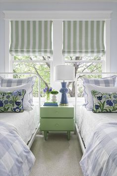 two twin beds in a bedroom with green nightstands and striped roman shades on the windows