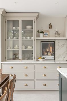 a kitchen with white cabinets and marble counter tops, along with wooden dining room chairs