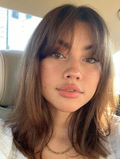 a young woman sitting in the back seat of a car wearing a white shirt and gold necklace