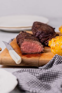 steak, corn on the cob and carrots are sitting on a cutting board