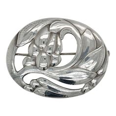 A fine antique Georg Jensen brooch or pin.  In sterling silver.  Model no. 65 with a floral motif.  Designed by Georg Jensen.  Together with its original box from Walter Muhke-Hofjuwelier Coblenz (Crown Jeweler).  Simply a wonderful brooch from one of Denmark's premier silversmiths!  Date: Early 20th Century  Overall Condition: It is in overall good, as-pictured, used estate condition.  Condition Details: There are two small spots of persistent tarnish to the reverse of the brooch. Otherwise, th Collectible Art Nouveau Hallmarked Brooch, Vintage White Gold Oval Brooches, Elegant Silver Brooch With Polished Finish, Art Deco Engraved Brooch For Formal Occasions, Art Deco Engraved Brooches For Formal Occasions, Art Deco Engraved Brooches For Formal Events, Classic Oval Silver Brooches, Antique Silver Brooch For Formal Occasions, Antique Silver Brooches For Formal Occasions