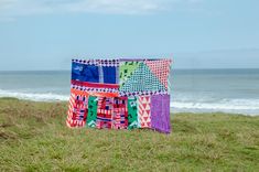 a patchwork quilt sitting on top of a lush green field next to the ocean