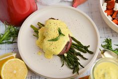 a white plate topped with asparagus covered in hollandaise sauce and surrounded by other foods