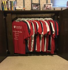 a bunch of red shirts hanging on a rack in a room next to a book shelf