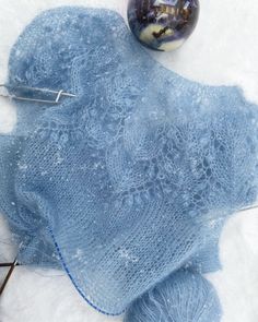 a blue knitted blanket next to a ball of yarn and needles on the snow