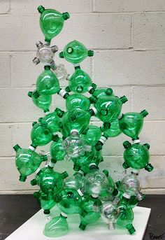 a sculpture made out of green glass bottles sitting on top of a white table next to a brick wall