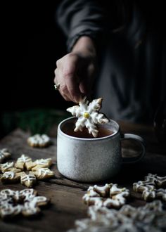 a person is dipping some sugar into a cup filled with star shaped cookies on a wooden table