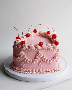 a pink cake with cherries on top sitting on a plate