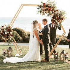 a bride and groom kissing in front of their wedding arch with flowers on the grass