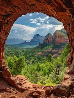 the view from inside a cave looking at mountains and trees