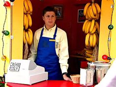 a man standing in front of a counter with bananas hanging from it's sides