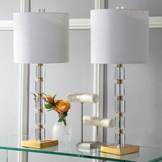 two lamps sitting on top of a glass table next to a vase with flowers in it