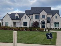 a large white brick house with a for sale sign in front of it on a cloudy day