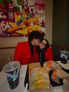 a man and woman sitting at a table with food in front of them, looking into each other's eyes