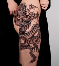 a woman with a dragon tattoo on her arm and leg, holding onto the side of her thigh