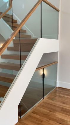 a stair case with glass railing and wood handrails in an empty room next to a wooden floor