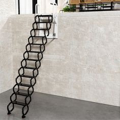 a black metal ladder sitting on top of a cement floor next to a white wall