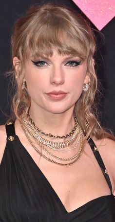 taylor swift is wearing a black dress with gold chains around her neck