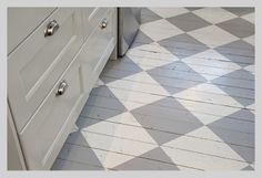 the kitchen floor is painted white and has checkerboard pattern on it, while the cabinets are off to the side