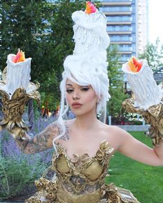 a woman with white hair is dressed in gold and has flowers on her head as she holds up two vases