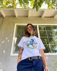 a woman standing in front of a window wearing a white t - shirt and blue pants