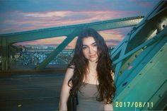 a woman standing in front of a bridge at sunset