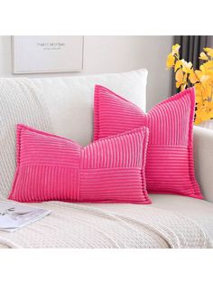 two pink pillows sitting on top of a white couch next to a vase with yellow flowers