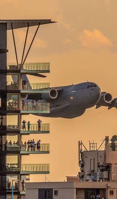 an airplane that is flying in the sky over some buildings and people are standing on balconies